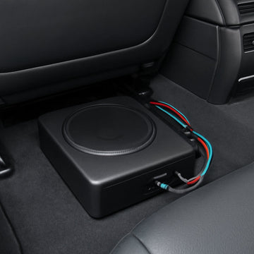 A sleek car interior showing a compact subwoofer box tucked under a seat, with a visible LOC and clean wiring. Alt: Assessing factory stereo compatibility for subwoofer installation