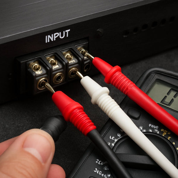 A close‑up of a car audio amplifier’s input terminals and RCA cables, showing a multimeter probe measuring voltage. Alt: "measuring amp input signal voltage for gain setting"