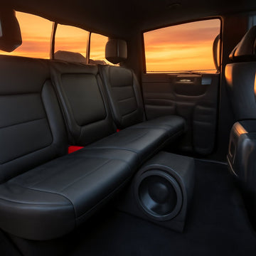 A sleek pickup truck interior at sunset, showing a custom‑mounted ported subwoofer box with a visible vent tube under the rear seat. Alt: ported subwoofer box installation in a truck, enhancing bass performance.