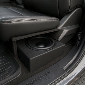 A photorealistic view of a Ford Super Duty interior showing an under‑seat subwoofer box installed beside the seat cushion, highlighting the limited clearance and acoustic baffle. Alt: Underseat subwoofer placement in Ford Super Duty truck.