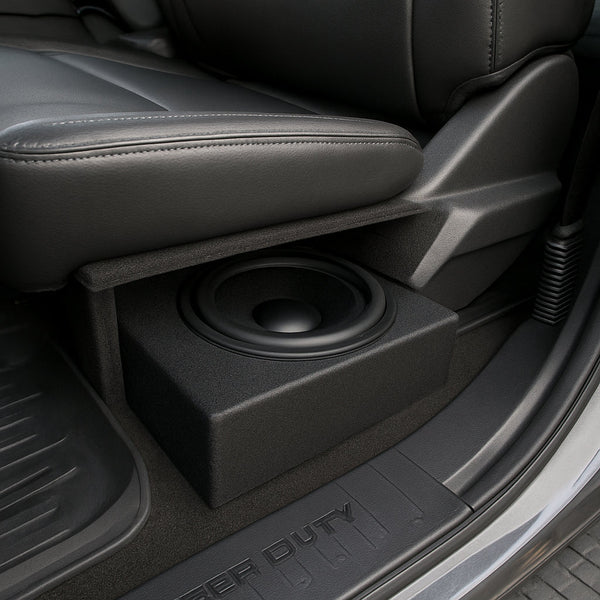 A photorealistic view of a Ford Super Duty interior showing an under‑seat subwoofer box installed beside the seat cushion, highlighting the limited clearance and acoustic baffle. Alt: Underseat subwoofer placement in Ford Super Duty truck.