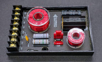 Electronic component board with red and silver coils, capacitors, and connectors on a dark background
