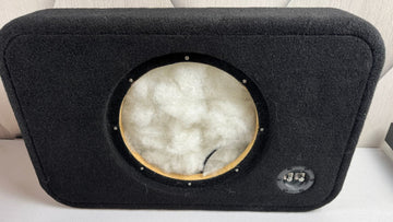 Car audio subwoofer enclosure with a visible brand logo on a white surface.