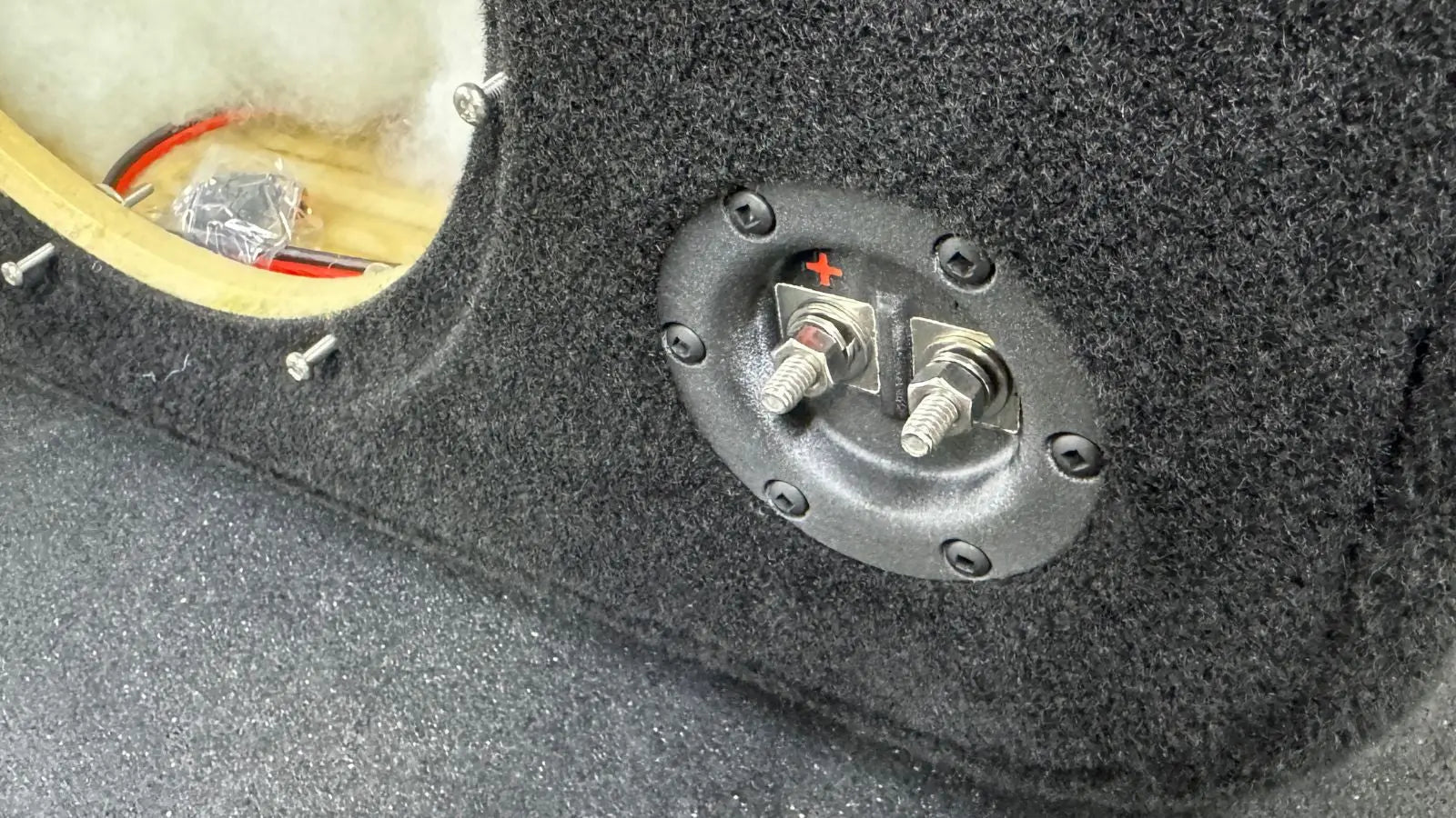 Close-up of a car audio subwoofer enclosure with wiring and connectors.