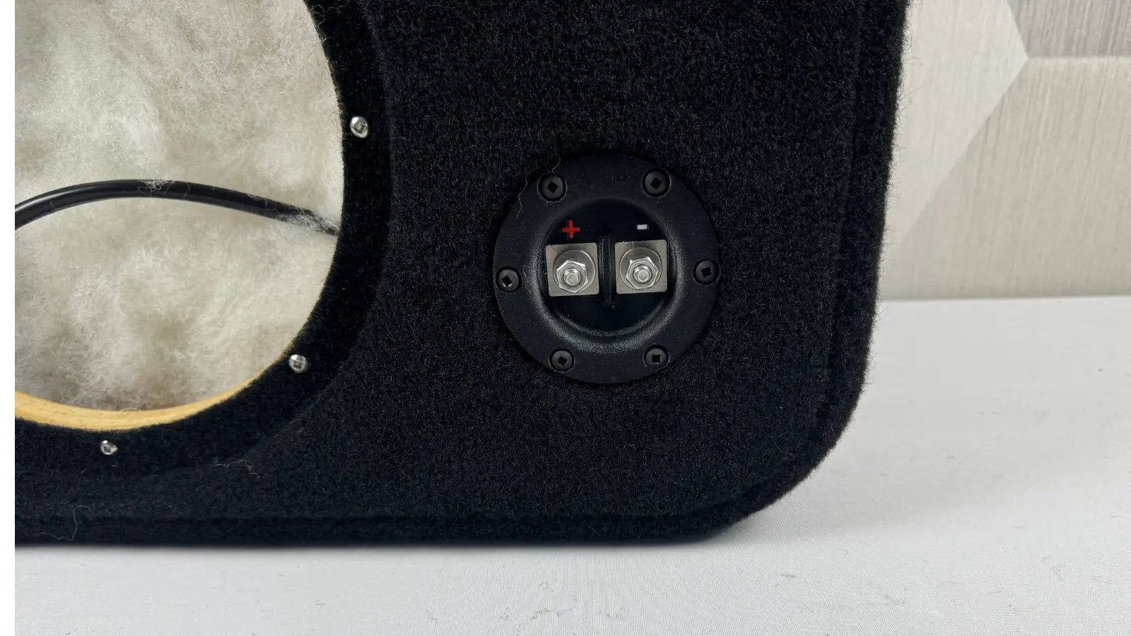 Close-up of a black car audio enclosure with wiring and connectors on a white surface.
