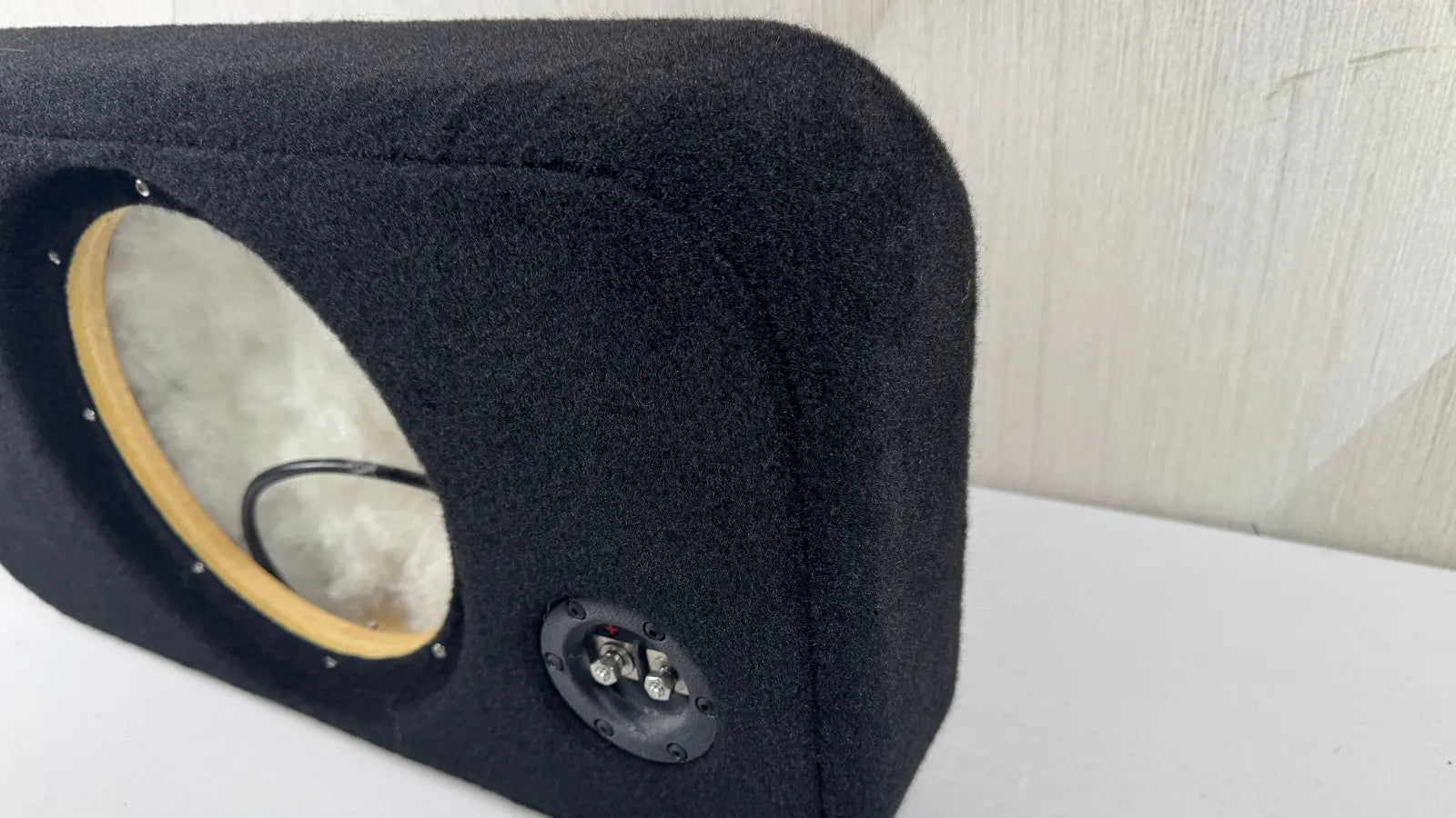 Black car speaker enclosure with visible driver and subwoofer on a white surface.