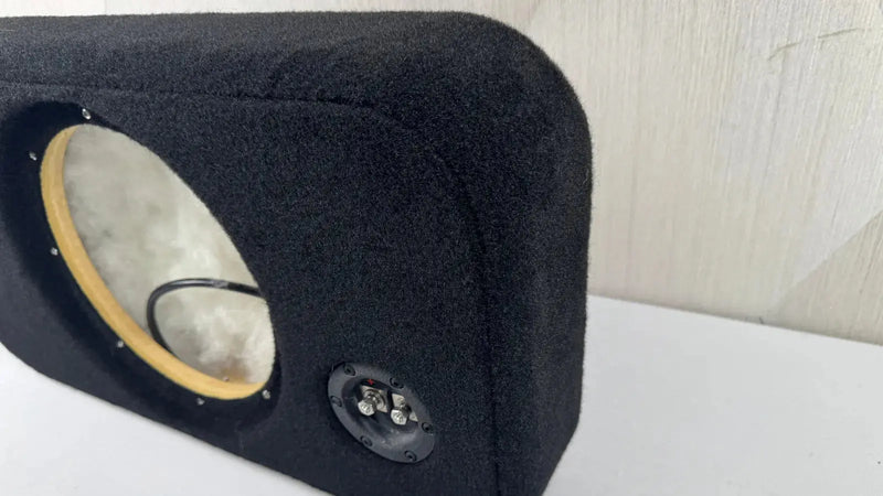 Black car speaker enclosure with visible driver and subwoofer on a white surface.